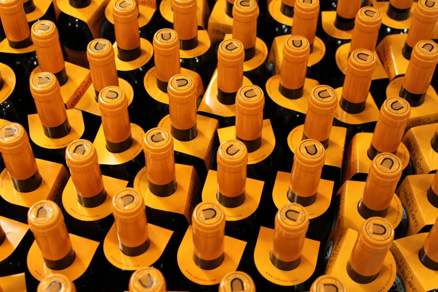 Garrafas de vinho empilhadas em uma adega, com rolhas amarelas visíveis.