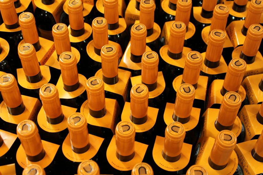 Garrafas de vinho empilhadas em uma adega, com rolhas amarelas visíveis.
