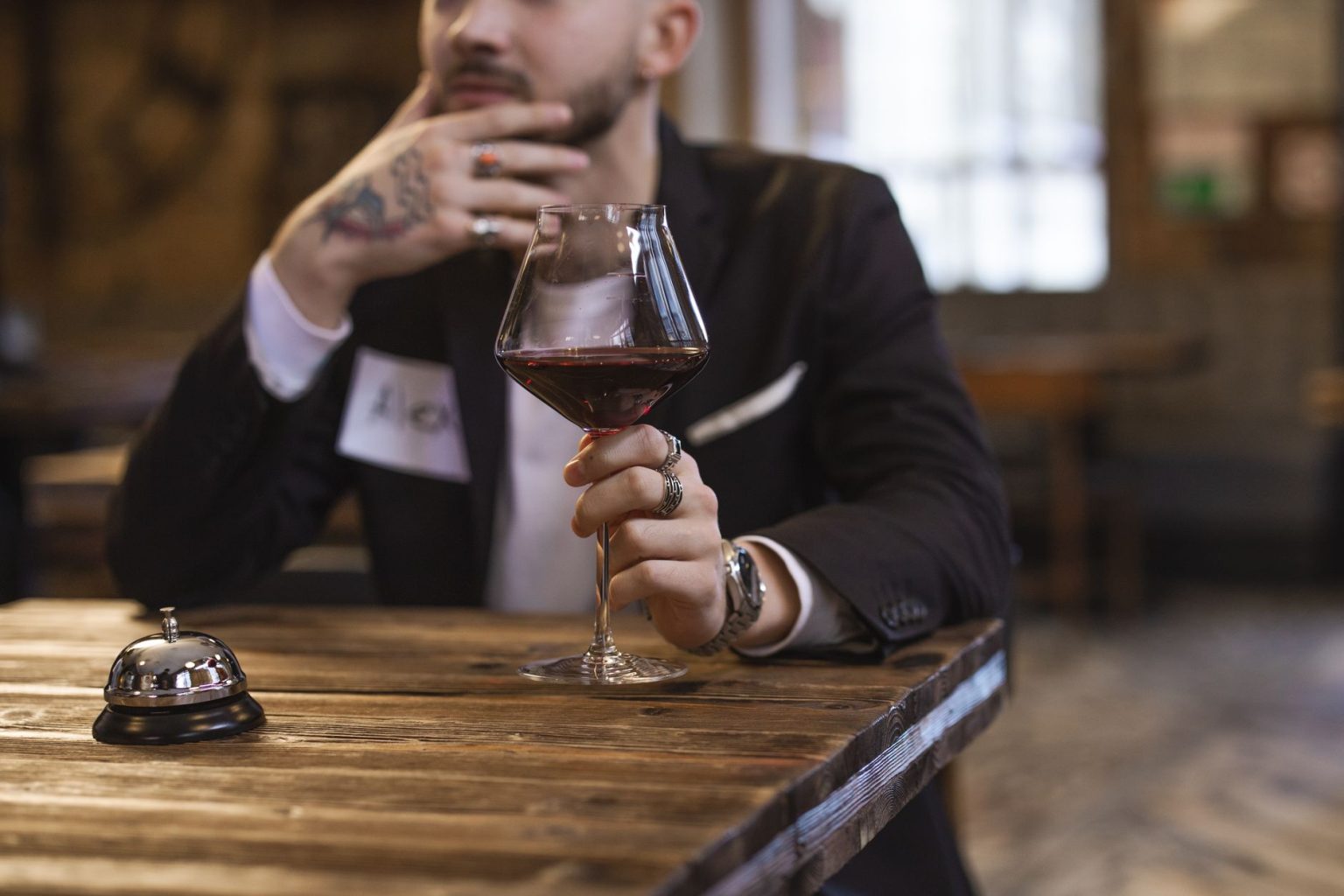 Homem de terno e crachá segura uma taça de vinho diante de uma mesa de degustação em ambiente interno.
