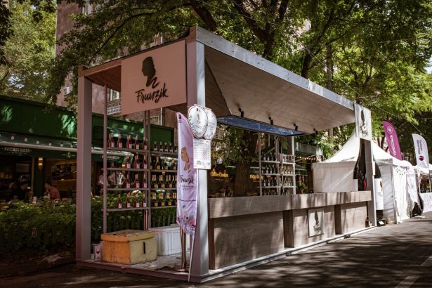 Barraca de vinhos em um mercado ao ar livre, cercada por árvores e movimentação de visitantes.