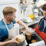 Dois trabalhadores preparam pedidos para entrega em uma pequena cozinha de restaurante.