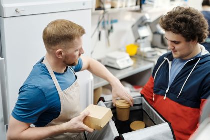 Dois trabalhadores preparam pedidos para entrega em uma pequena cozinha de restaurante.