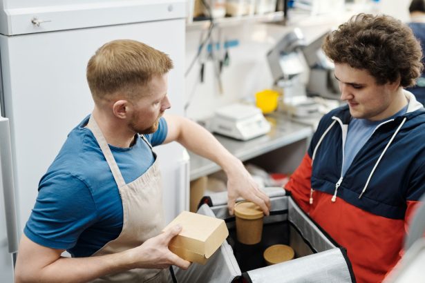 Dois trabalhadores preparam pedidos para entrega em uma pequena cozinha de restaurante.